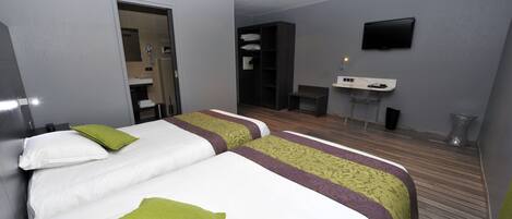 Habitación de hotel con dos camas, un escritorio pequeño, un televisor y un baño visible a través de una puerta abierta.