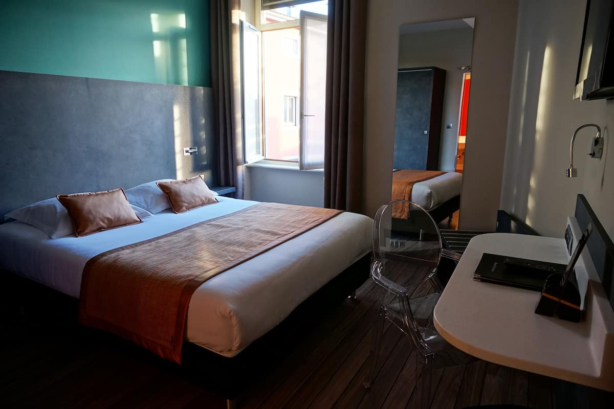 A hotel room with a bed, bedside table, and a mirror.