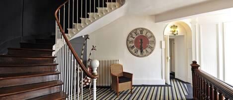 A staircase with wooden steps and a white railing, leading to a room with a large wall clock and a striped carpet.