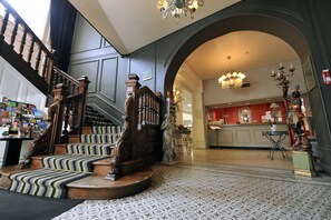Una imponente escalera con alfombra estampada, un candelabro y una estatua.