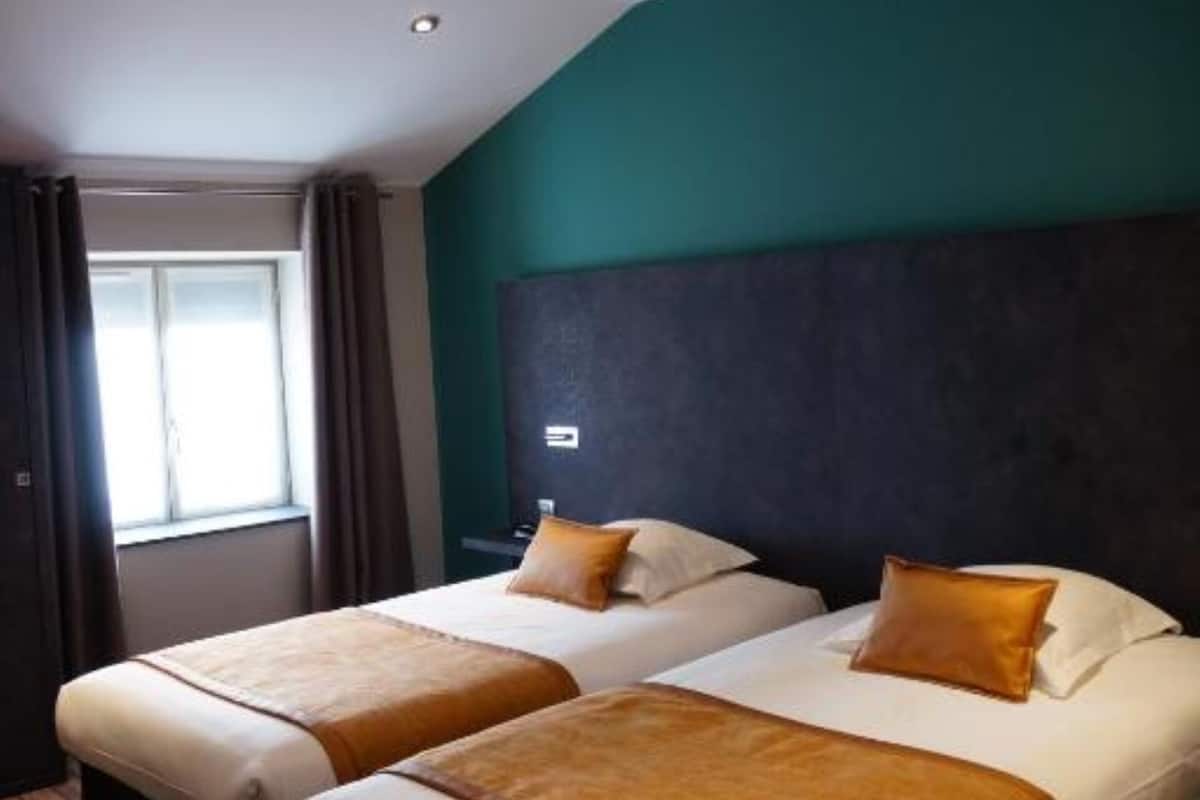 A hotel room with two beds, a dark headboard, a window with curtains, and a wooden floor.