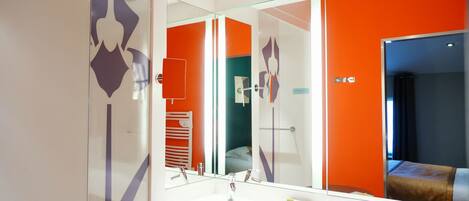 Un baño moderno con un espejo grande, un lavabo blanco y un mamparo de vidrio.