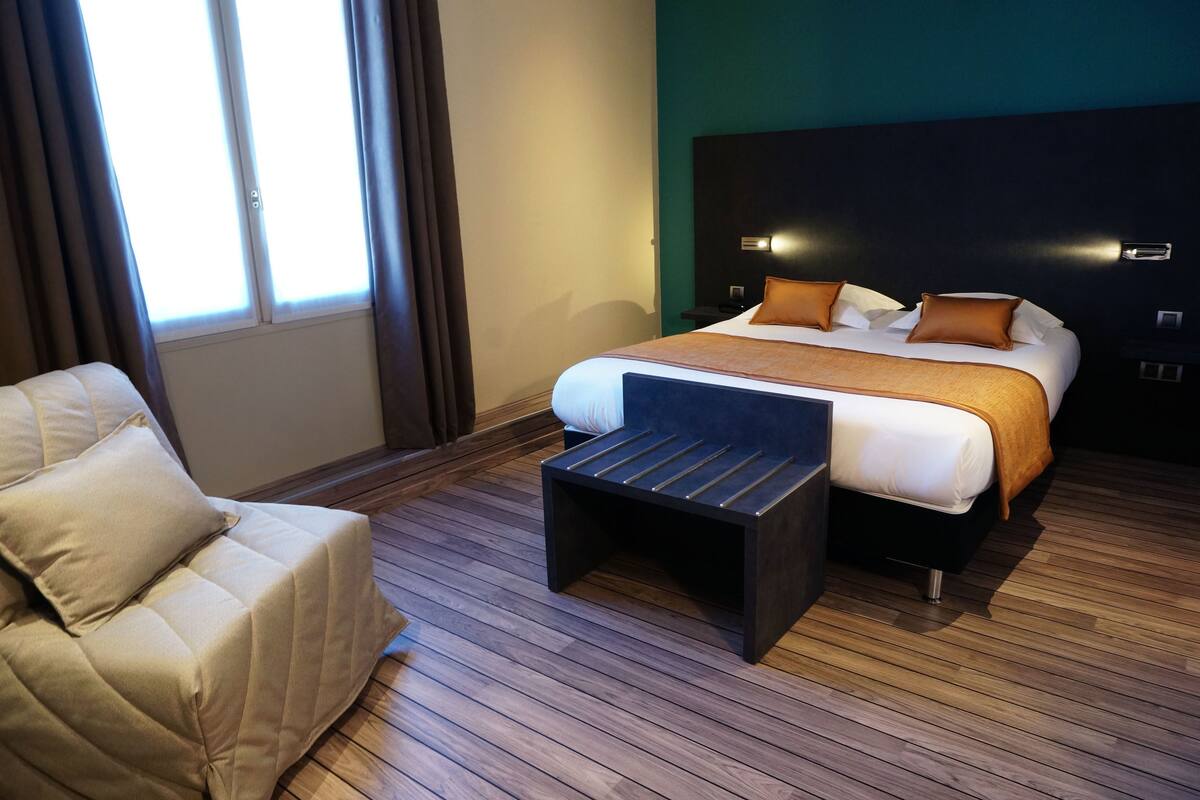 A modern hotel room with a large bed, a small sofa, and a wooden floor.