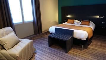 A modern hotel room with a large bed, a small sofa, and a wooden floor.