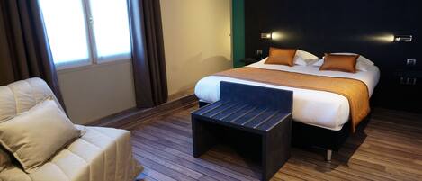 Una habitación de hotel moderna con una cama grande, un pequeño sofá y piso de madera.