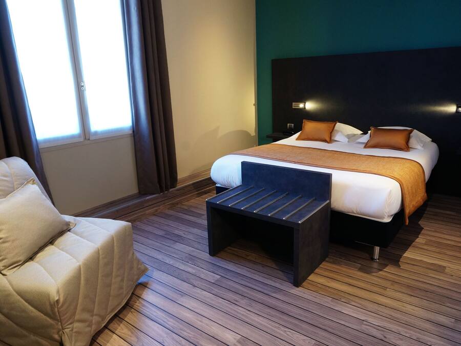A modern hotel room with a large bed, a small sofa, and a wooden floor.