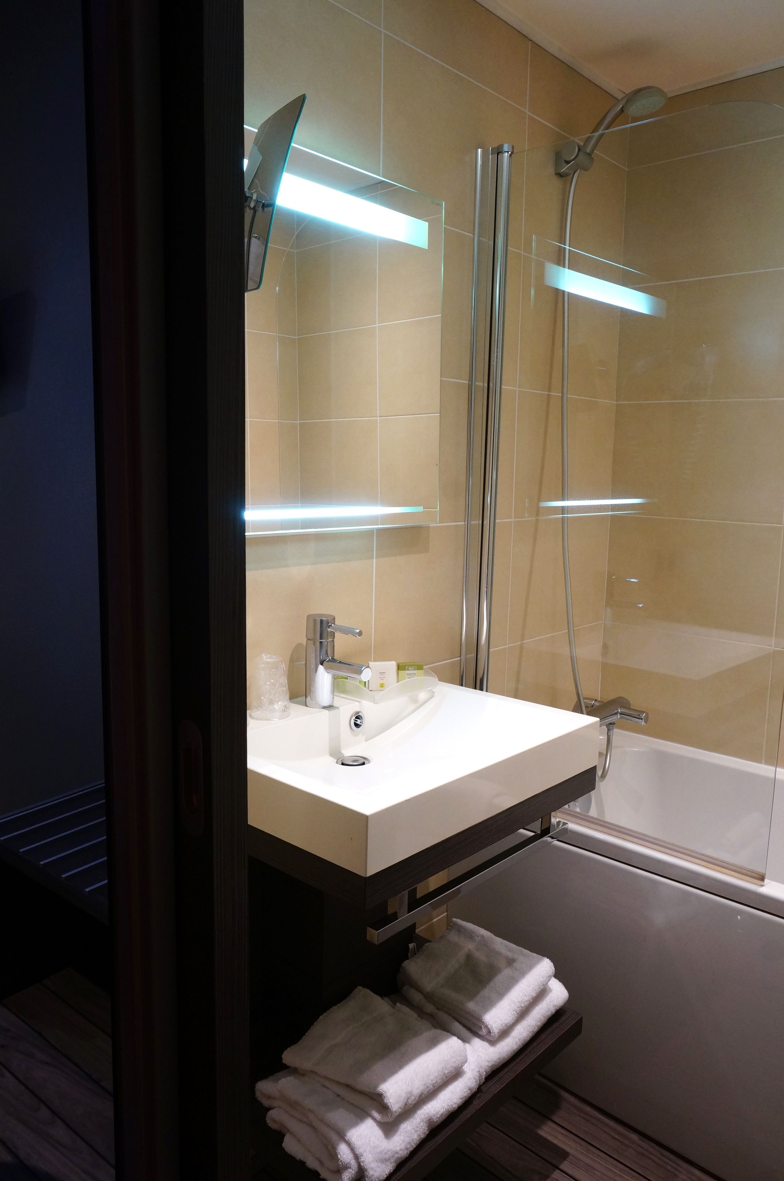 A modern bathroom with a white sink, a mirror, a handheld showerhead, and a bathtub.