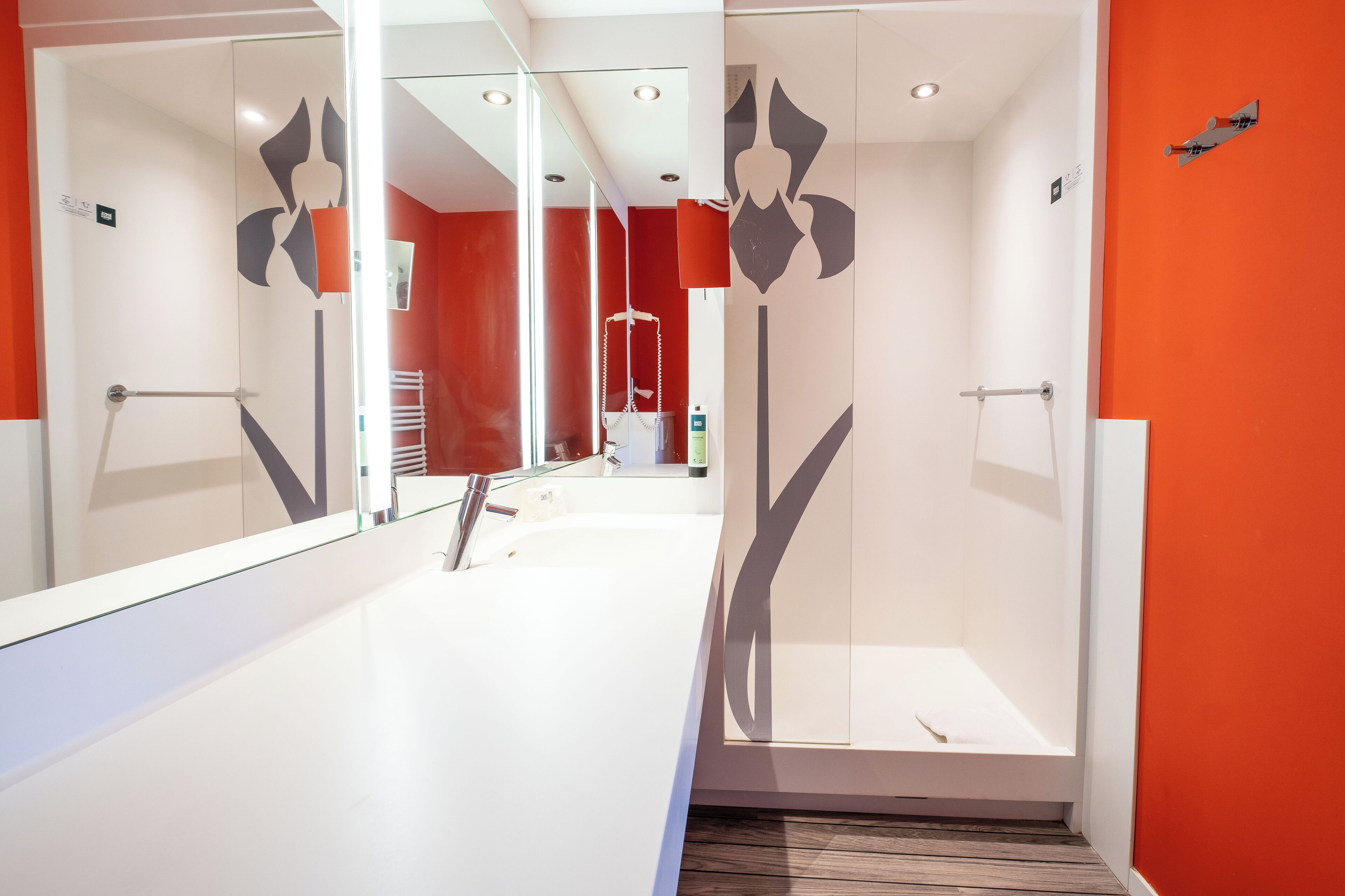 Un baño moderno con cabina de ducha de vidrio, un lavabo blanco y una pared de acento roja.
