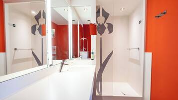 Un baño moderno con cabina de ducha de vidrio, un lavabo blanco y una pared de acento roja.