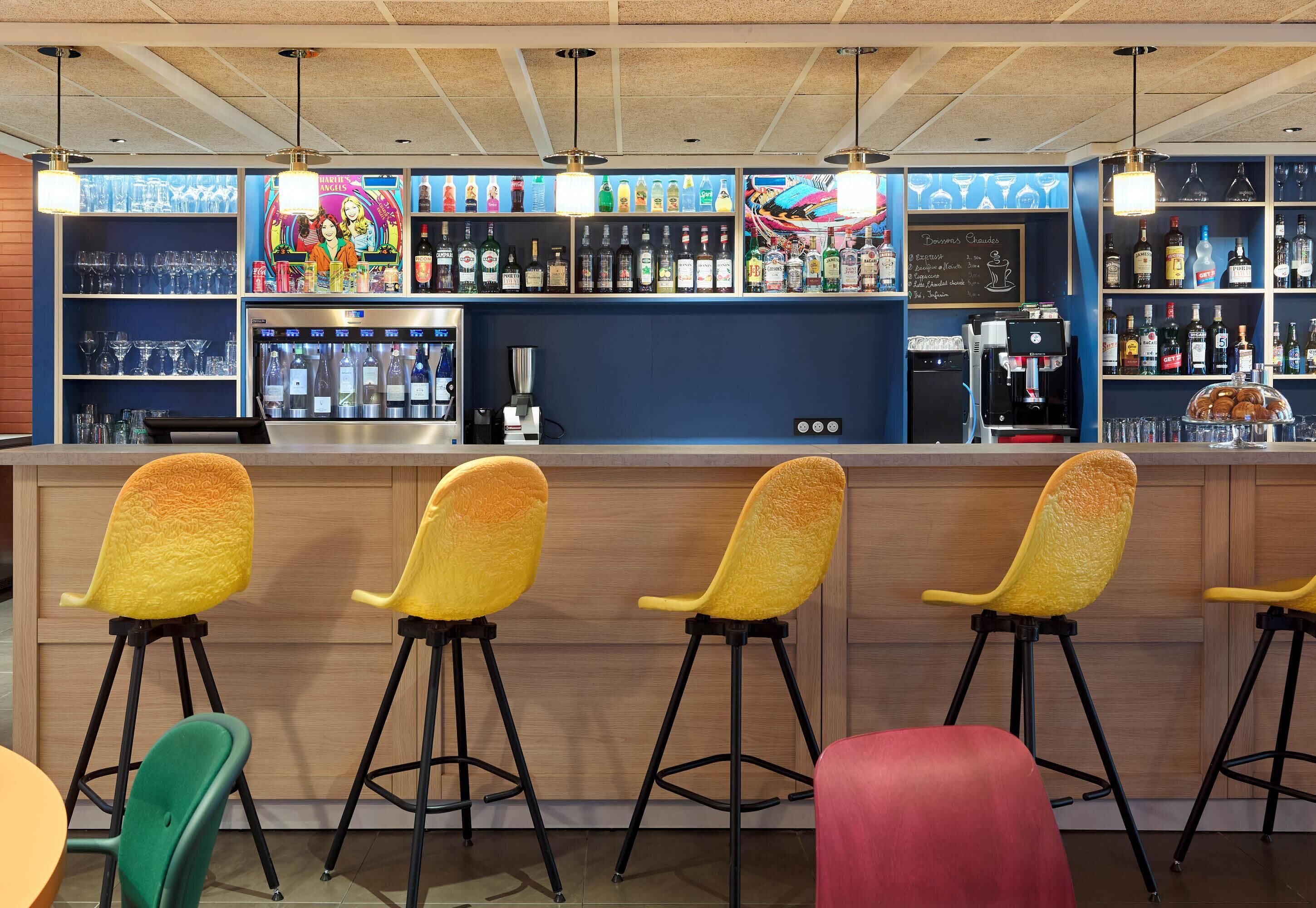 Una zona de bar con taburetes, estantes llenos de botellas y una máquina de café.