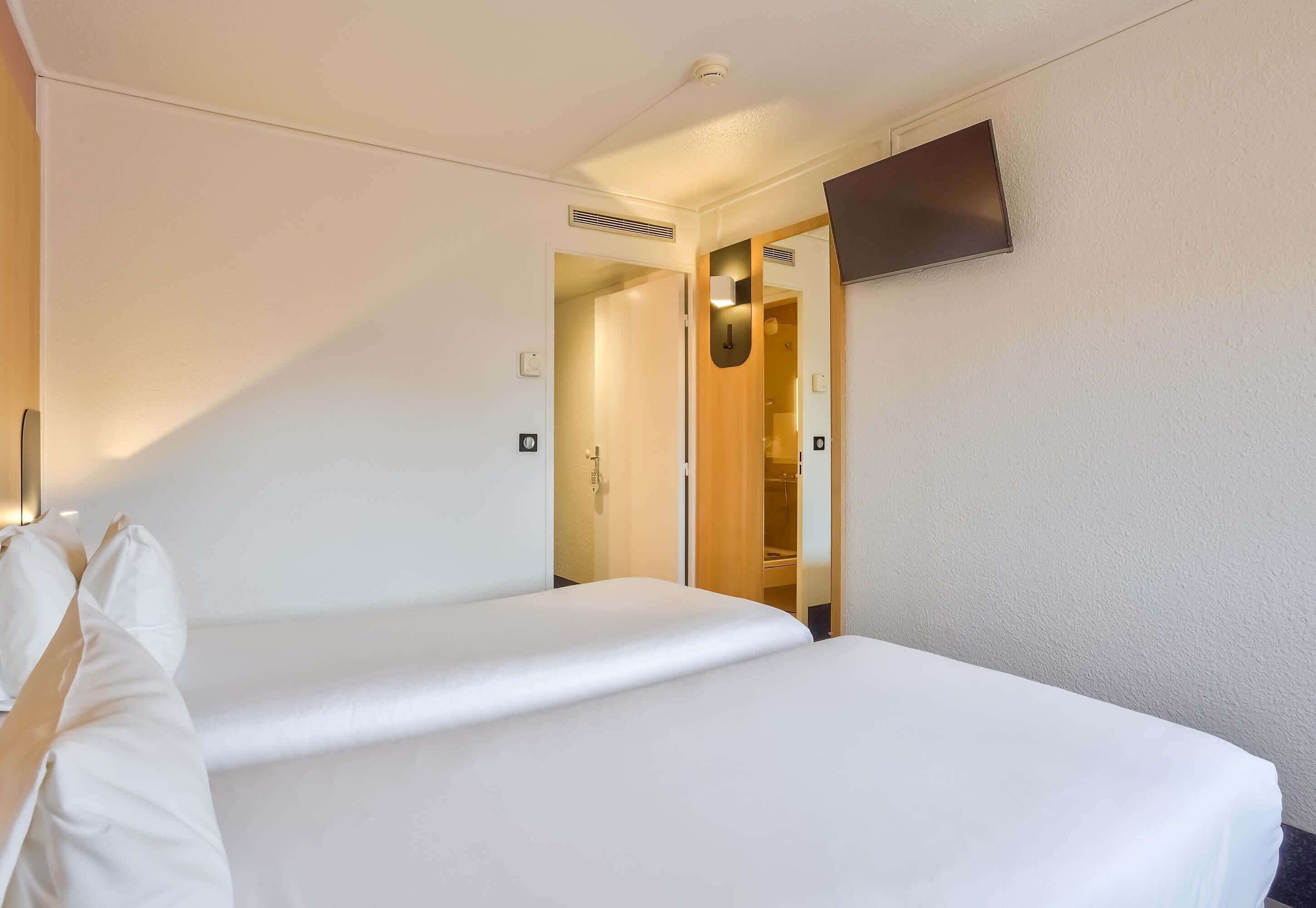 Une chambre d’hôtel avec un lit, un téléviseur fixé au mur et une porte donnant sur un placard.