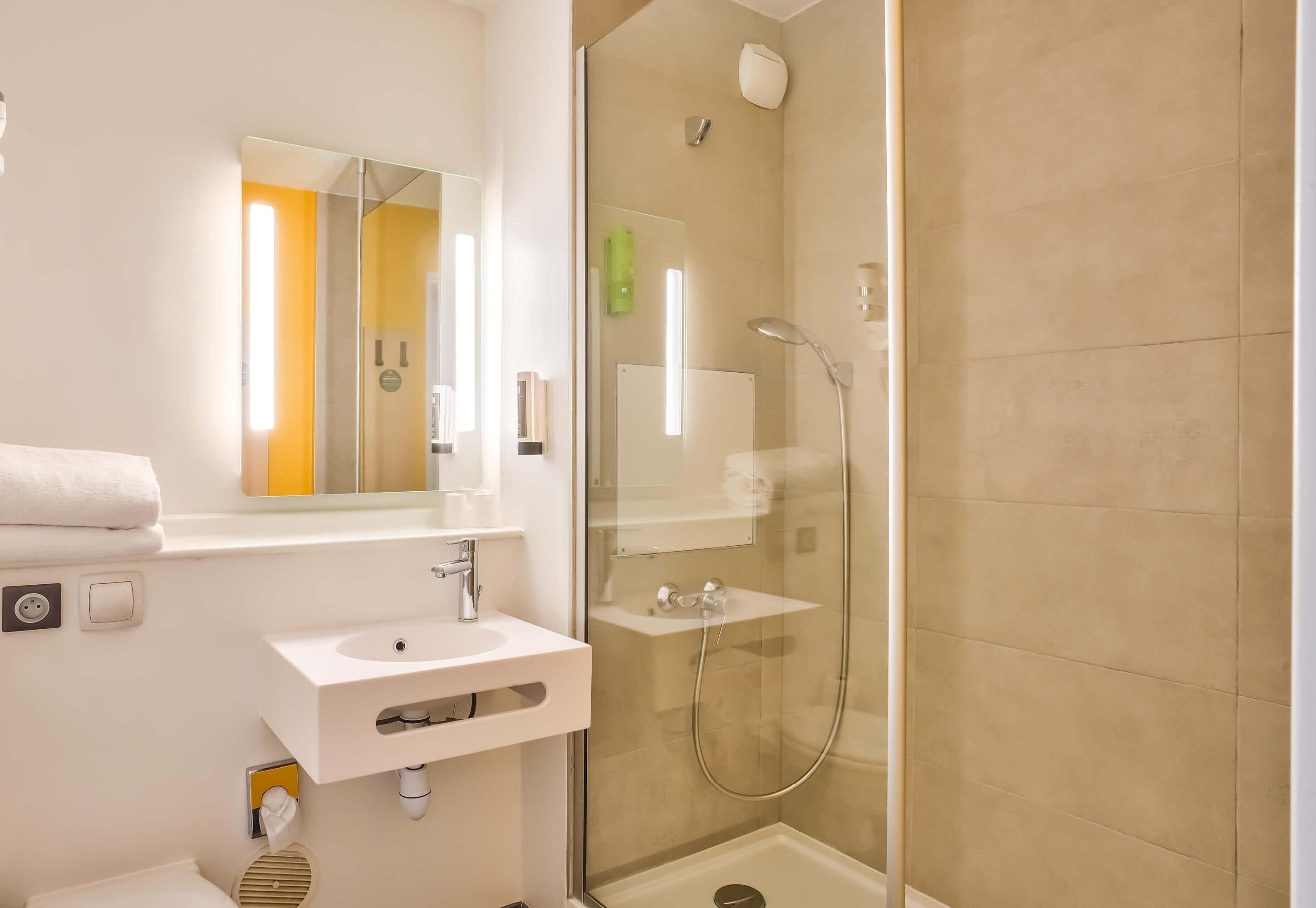 Un baño moderno con ducha envuelta en vidrio, lavabo blanco y espejo.