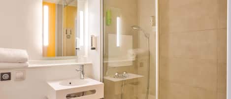 Un baño moderno con ducha envuelta en vidrio, lavabo blanco y espejo.