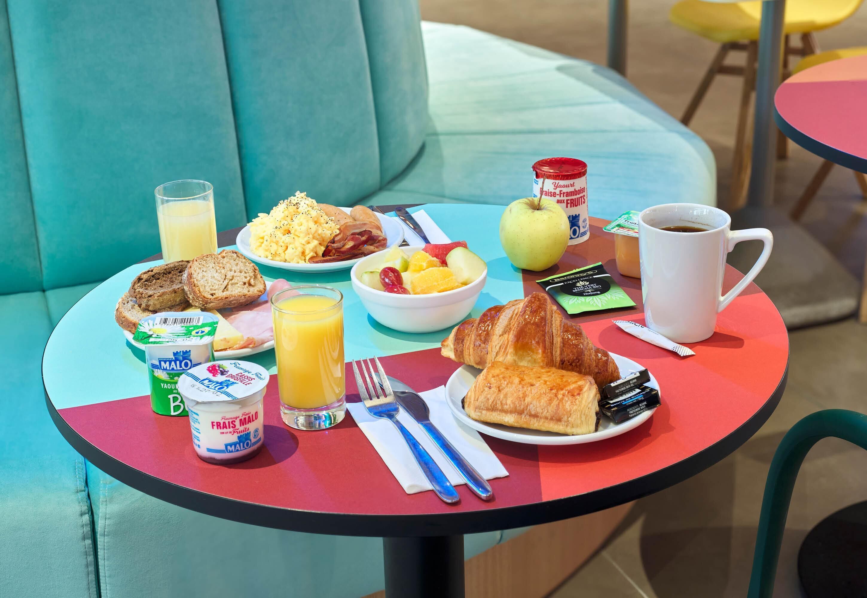 Une table de petit-déjeuner avec des croissants, du yaourt, des fruits, du jus et du café.