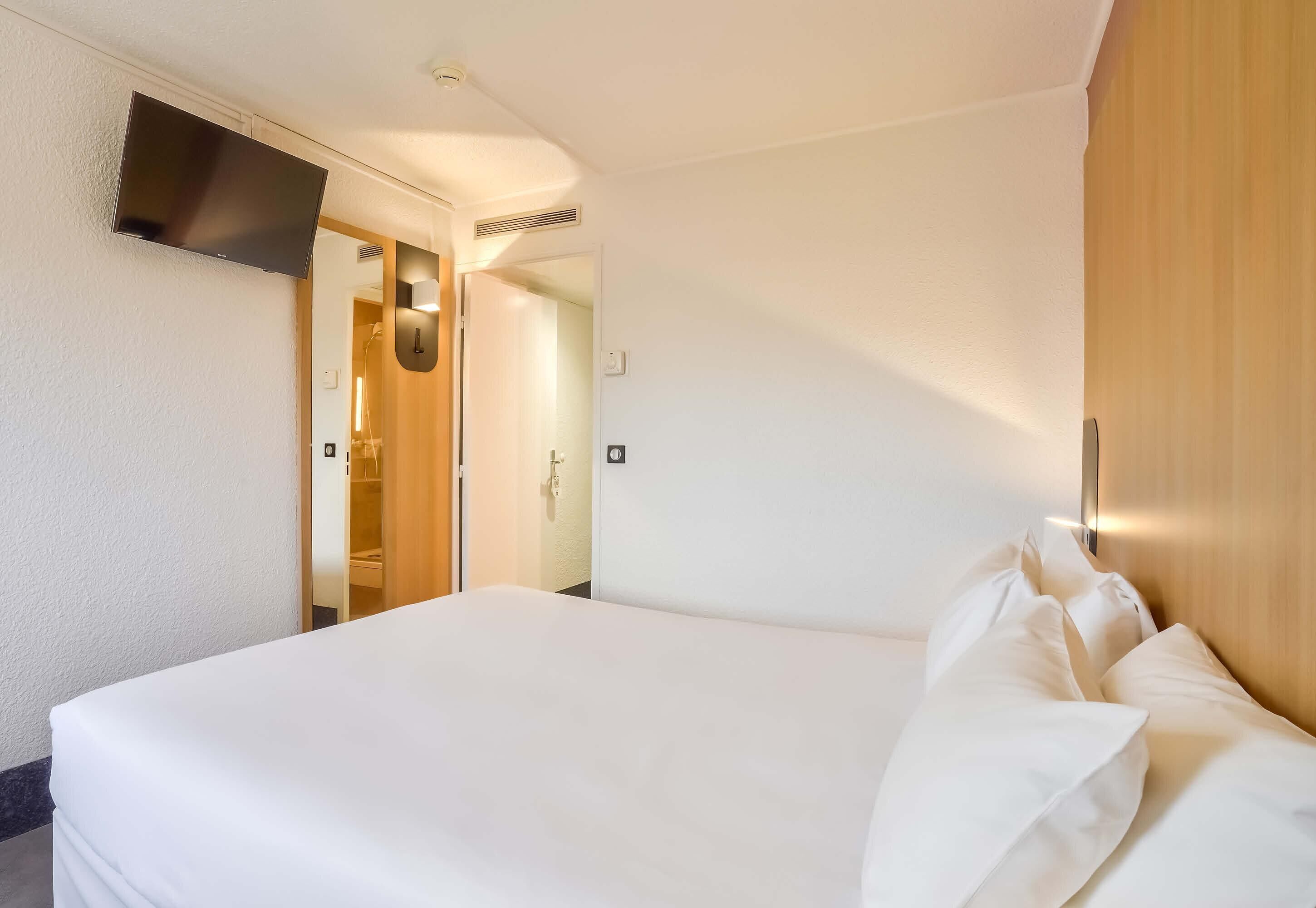 Une chambre d’hôtel avec un lit, un téléviseur fixé au mur et une armoire en bois.