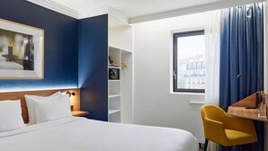 Ein Hotelzimmer mit Bett, Schreibtisch, Stuhl, Kleiderschrank und einem Fenster mit Vorhängen.