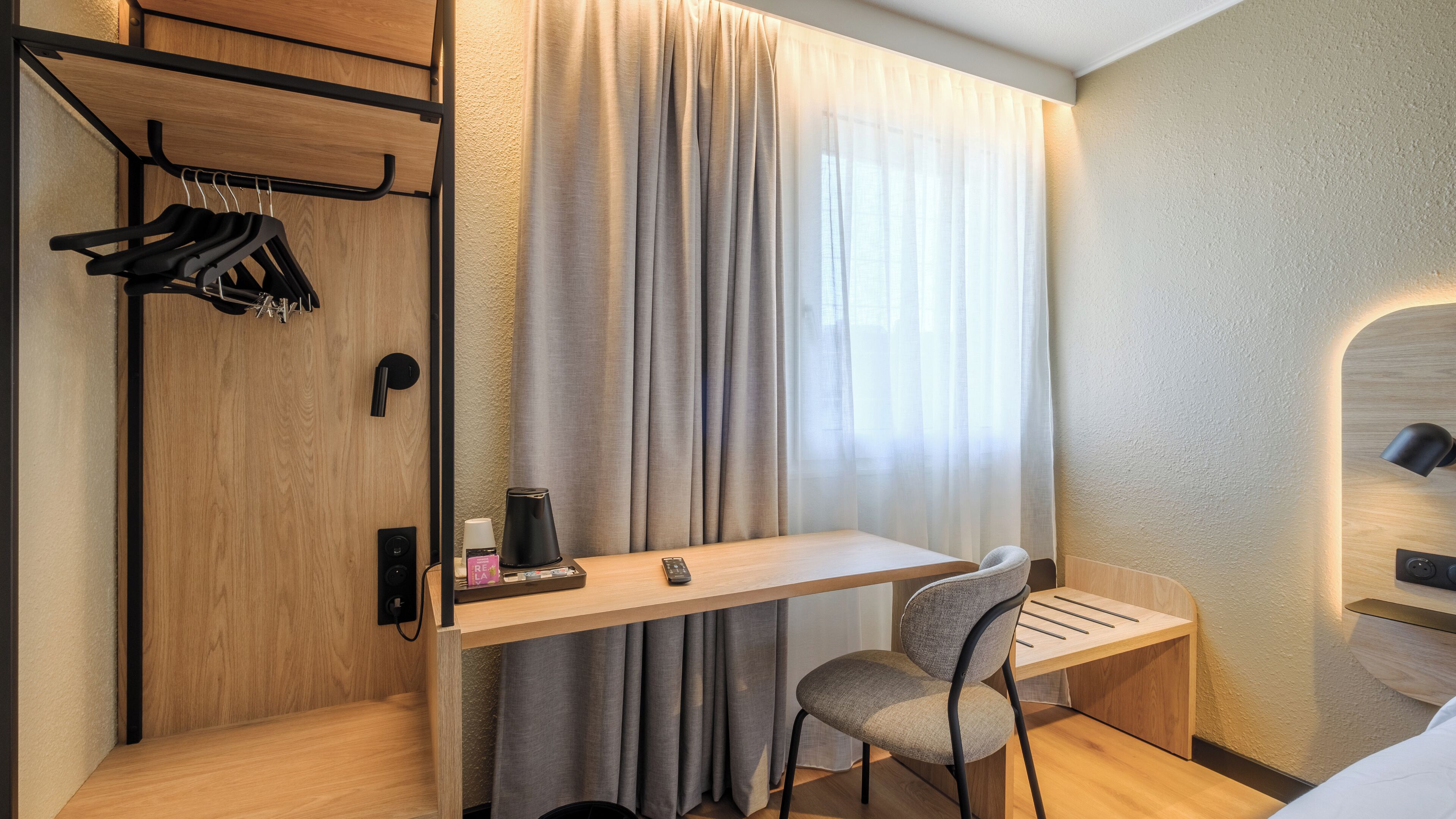 Una habitación de hotel compacta con un escritorio de madera, una silla, una mesita, un perchero y una cama.
