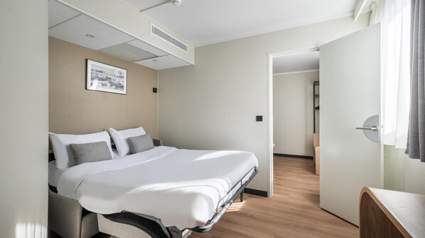 Una habitación de hotel moderna con una cama bien hecha, un escritorio pequeño y un cuadro en la pared.