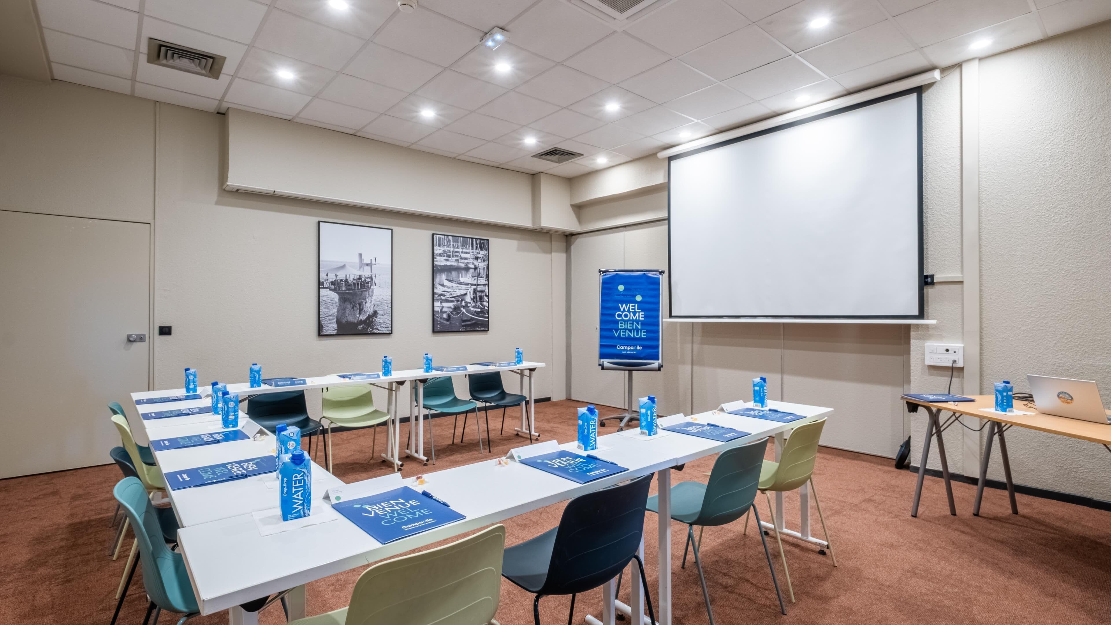 A conference room with tables, chairs, a projector screen, and a welcome banner.