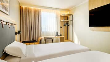 Habitación de hotel con cama, un escritorio con silla, televisor montado en la pared y perchero.