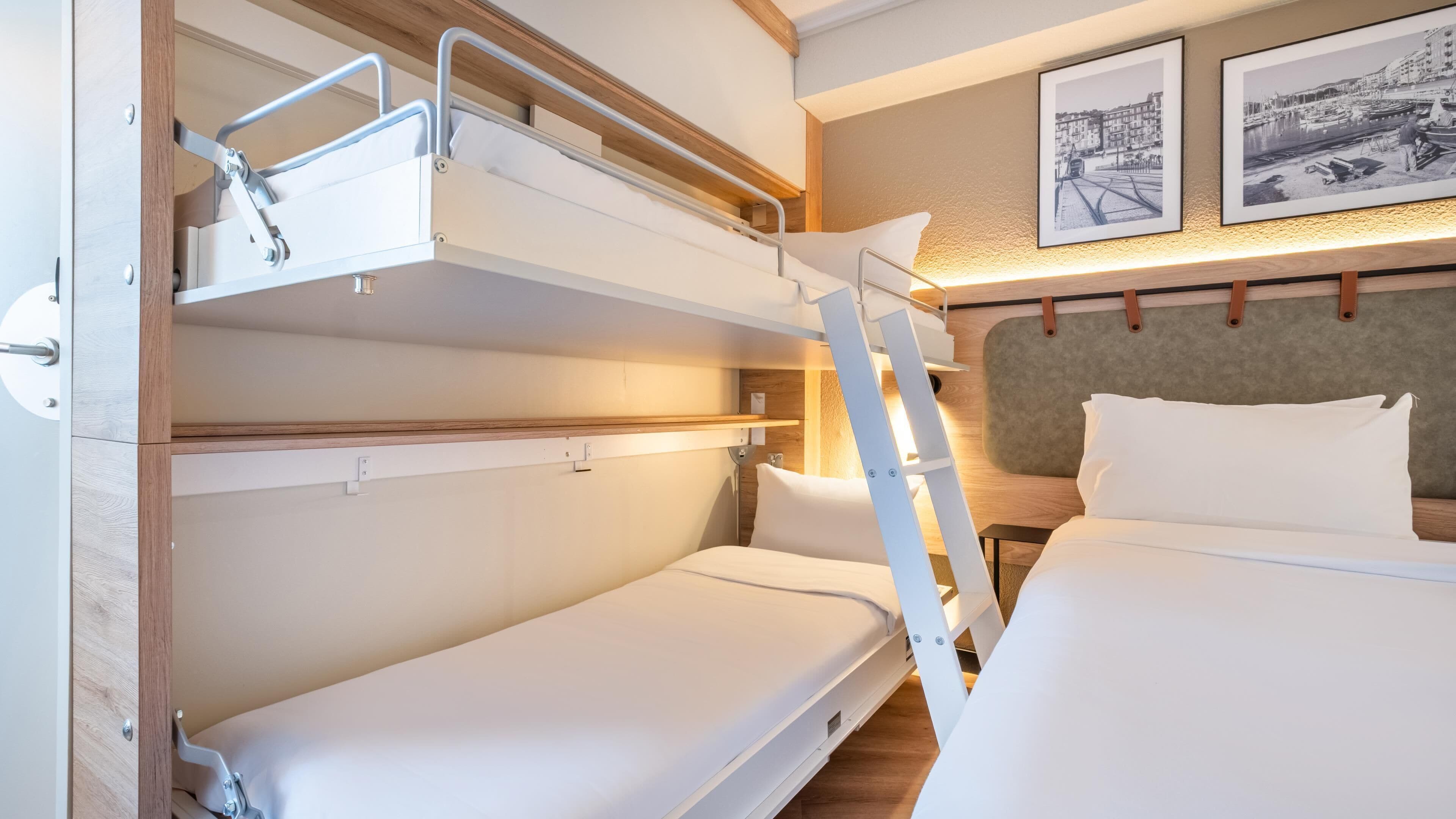 A bunk bed room with a ladder, a bed, and two framed pictures on the wall.