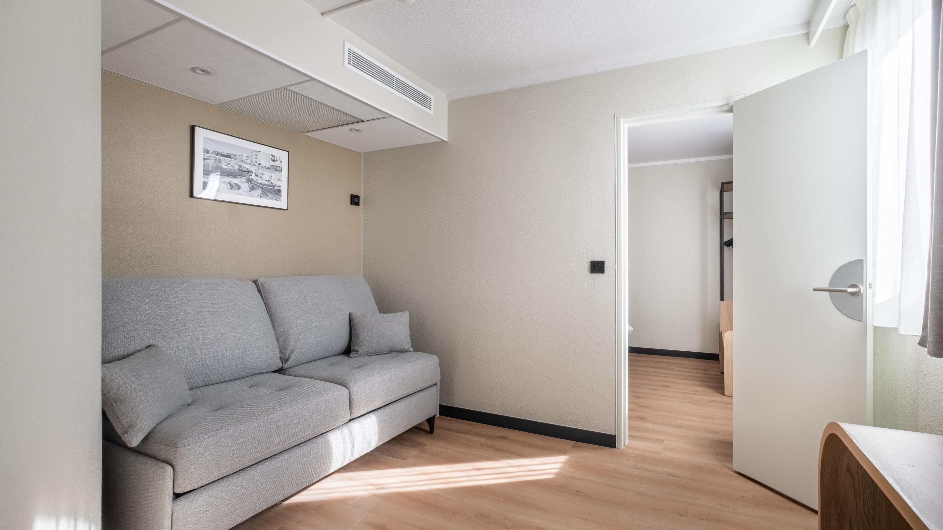 Un salon moderne et minimaliste, avec un canapé gris, un tableau encadré au mur et un plancher en bois.