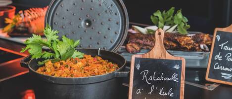 Un ambiente de restaurante con una olla negra de ratatouille, una tabla de madera con un menú en la pizarra y una bandeja de comida.