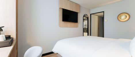A hotel room with a bed, a desk with a chair, a TV mounted on the wall, and a mirror.