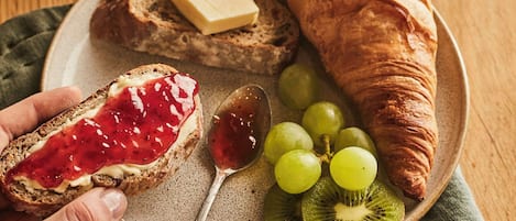 A breakfast plate with toast, a croissant, grapes, kiwi slices, and a glass of orange juice.