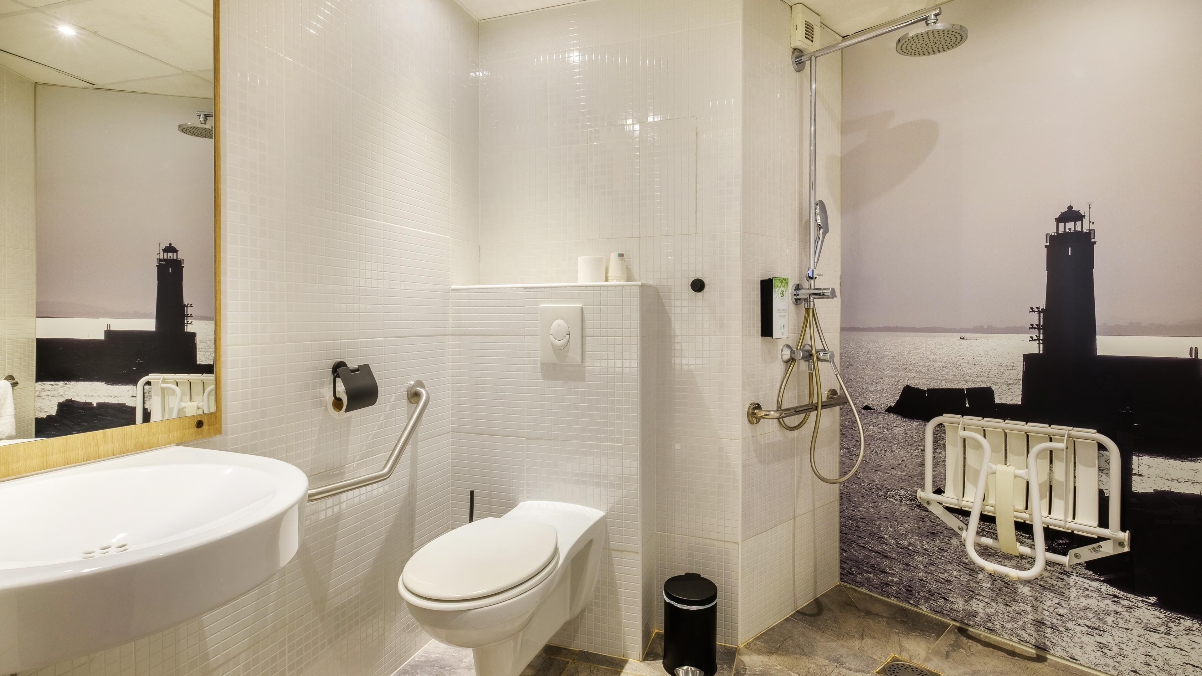 A modern bathroom with a white bathtub, a toilet, a shower with a glass door, and a handrail.