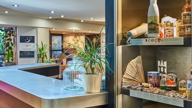 Un área de recepción con un mostrador moderno, una planta en maceta y una exhibición de varios objetos, incluyendo un abanico, una botella y un tarro.