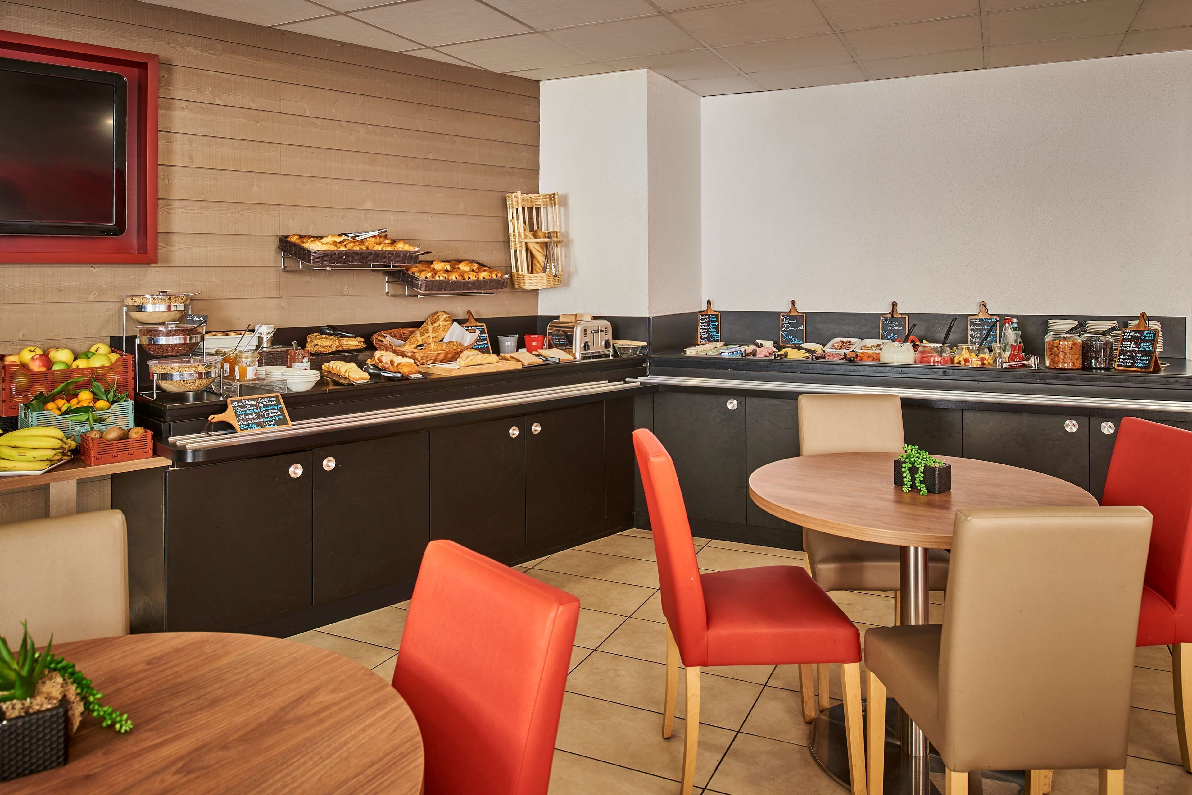 Zona de buffet con diferentes opciones de comida, una barra con menú en una pizarra y sillas rojas alrededor de una mesa de madera.