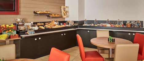 Zona de buffet con diferentes opciones de comida, una barra con menú en una pizarra y sillas rojas alrededor de una mesa de madera.