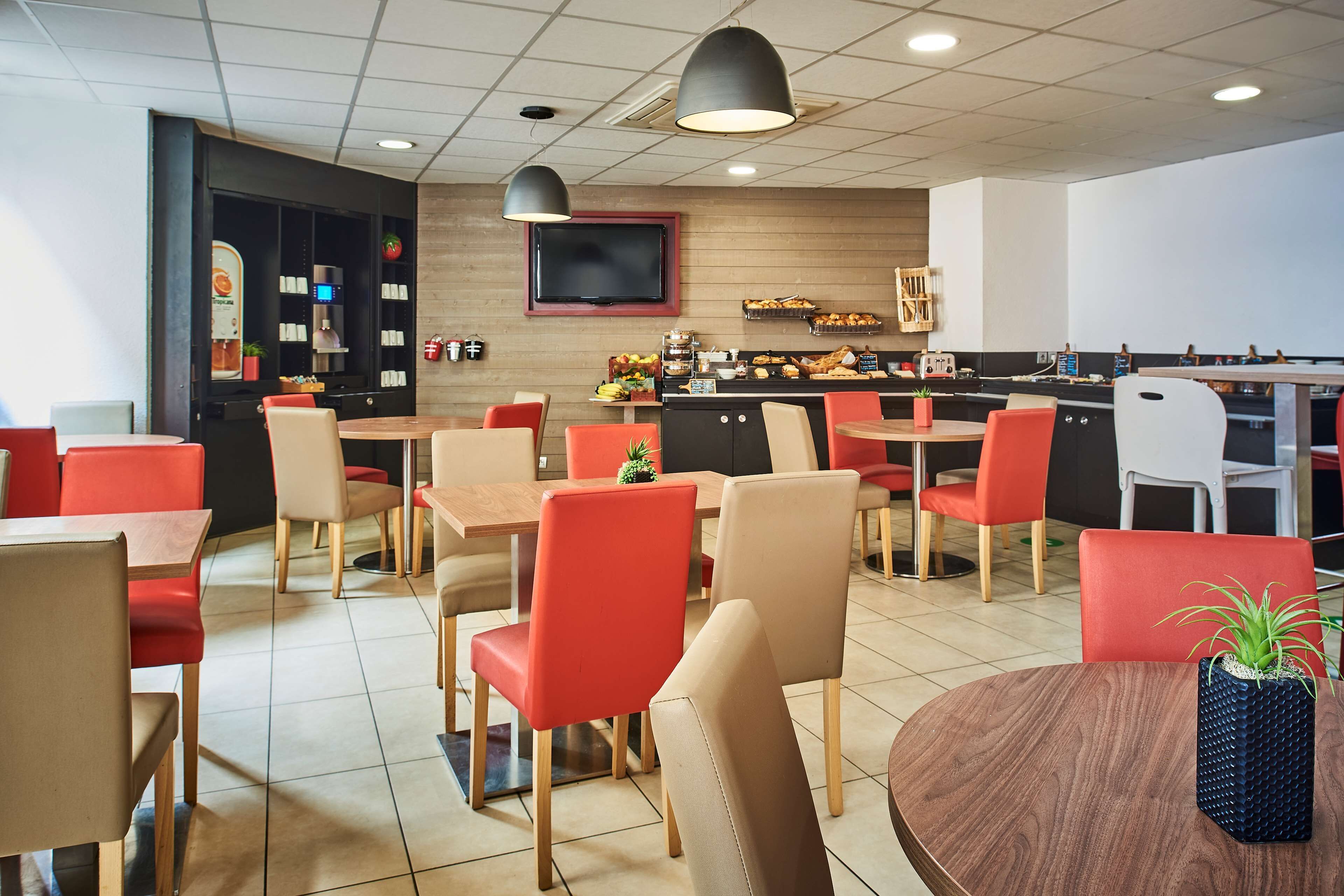 Een modern restaurant met rode en beige stoelen, houten tafels en een centraal bedieningsstation met etalages.
