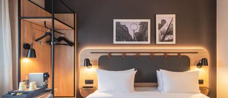 Habitación de hotel con una cama, lámparas de noche, un armario de madera, un escritorio con lámpara y dos cuadros en la pared.