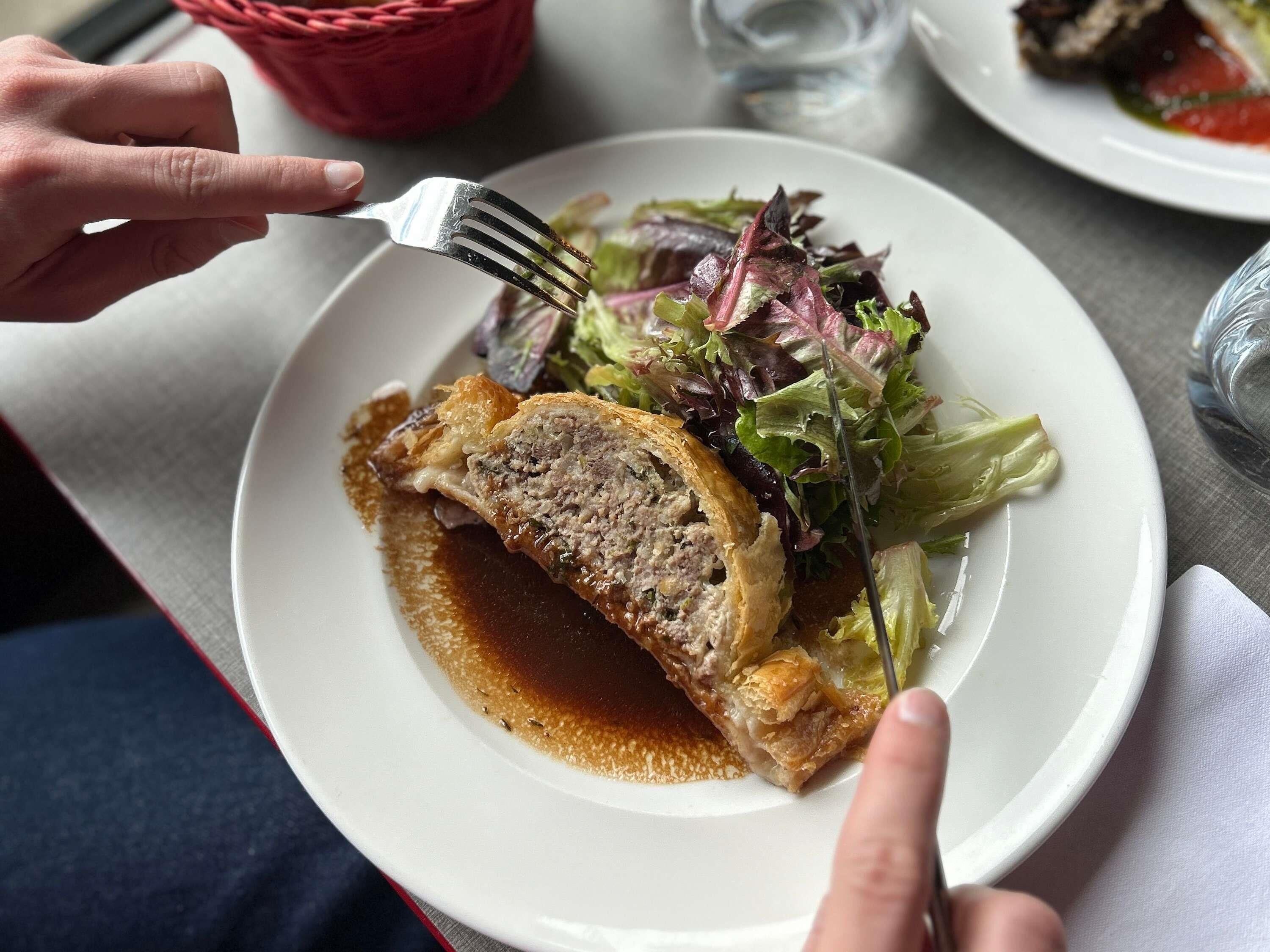 A plate with a meat dish and salad, a fork, and a napkin on a table.