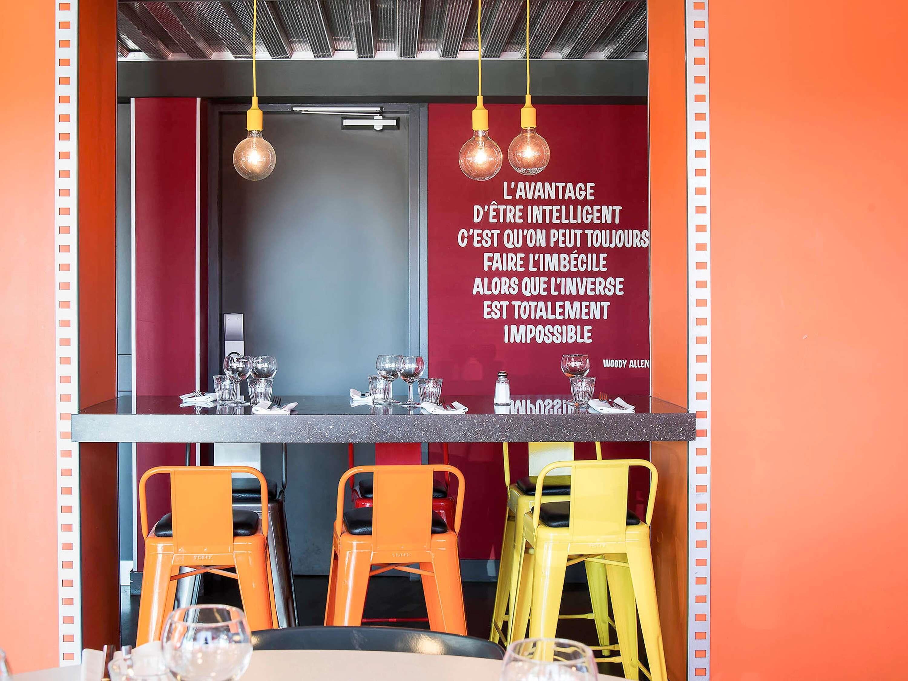 En restaurantindretning med barområde, røde og gule stole og et citat på væggen.