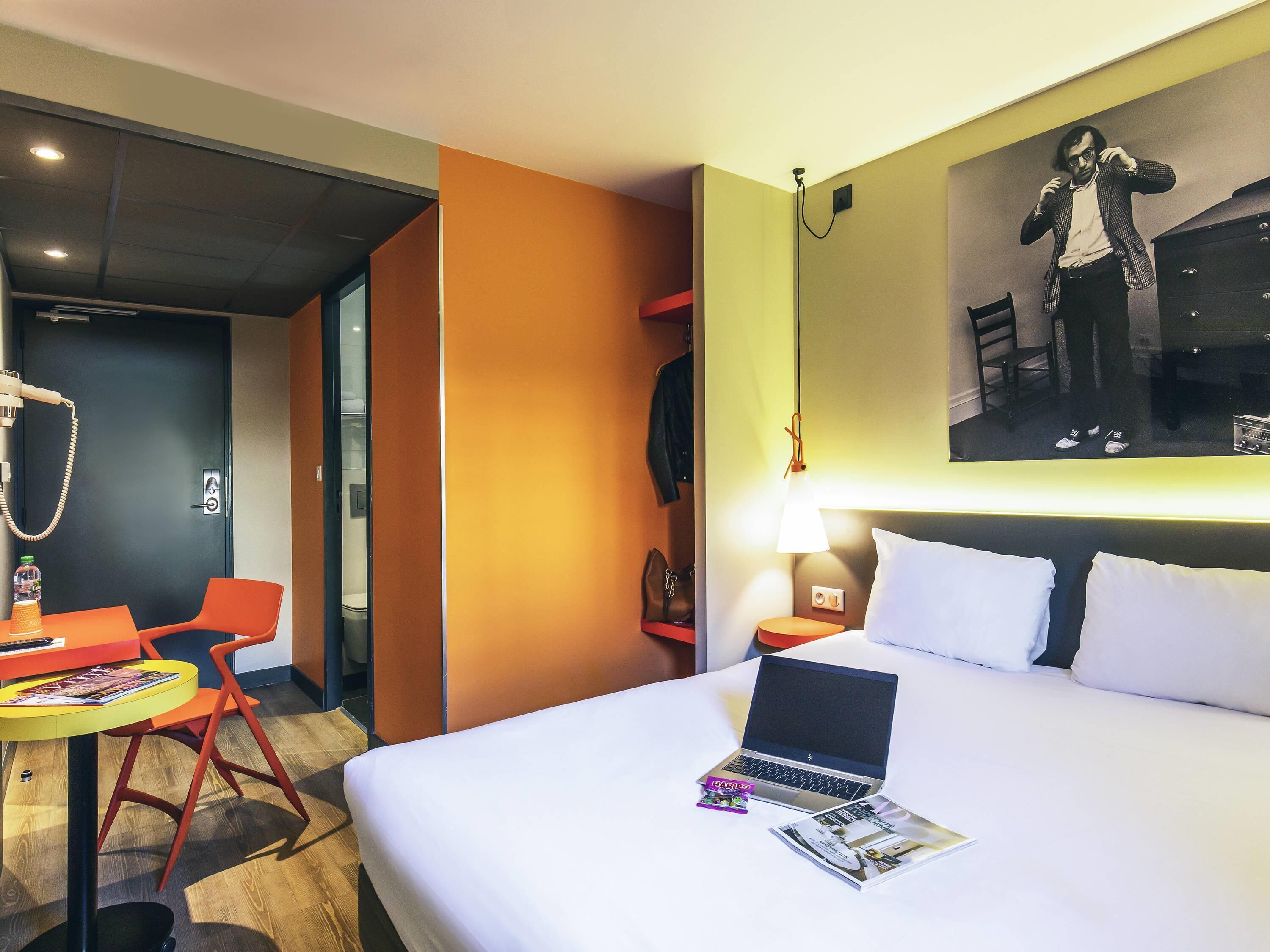 Een hotelkamer met een bed, een bureau met een laptop, een stoel en een lamp.