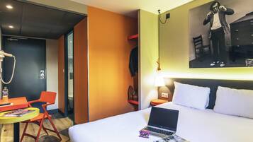 Een hotelkamer met een bed, een bureau met een laptop, een stoel en een lamp.
