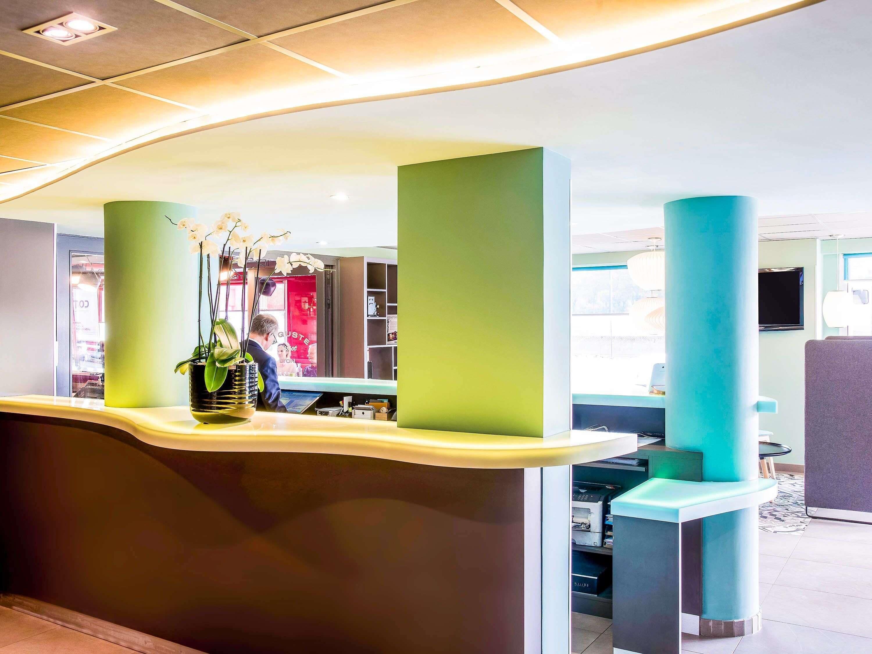 A reception area with a curved counter, a potted plant, and a red sign in the background.