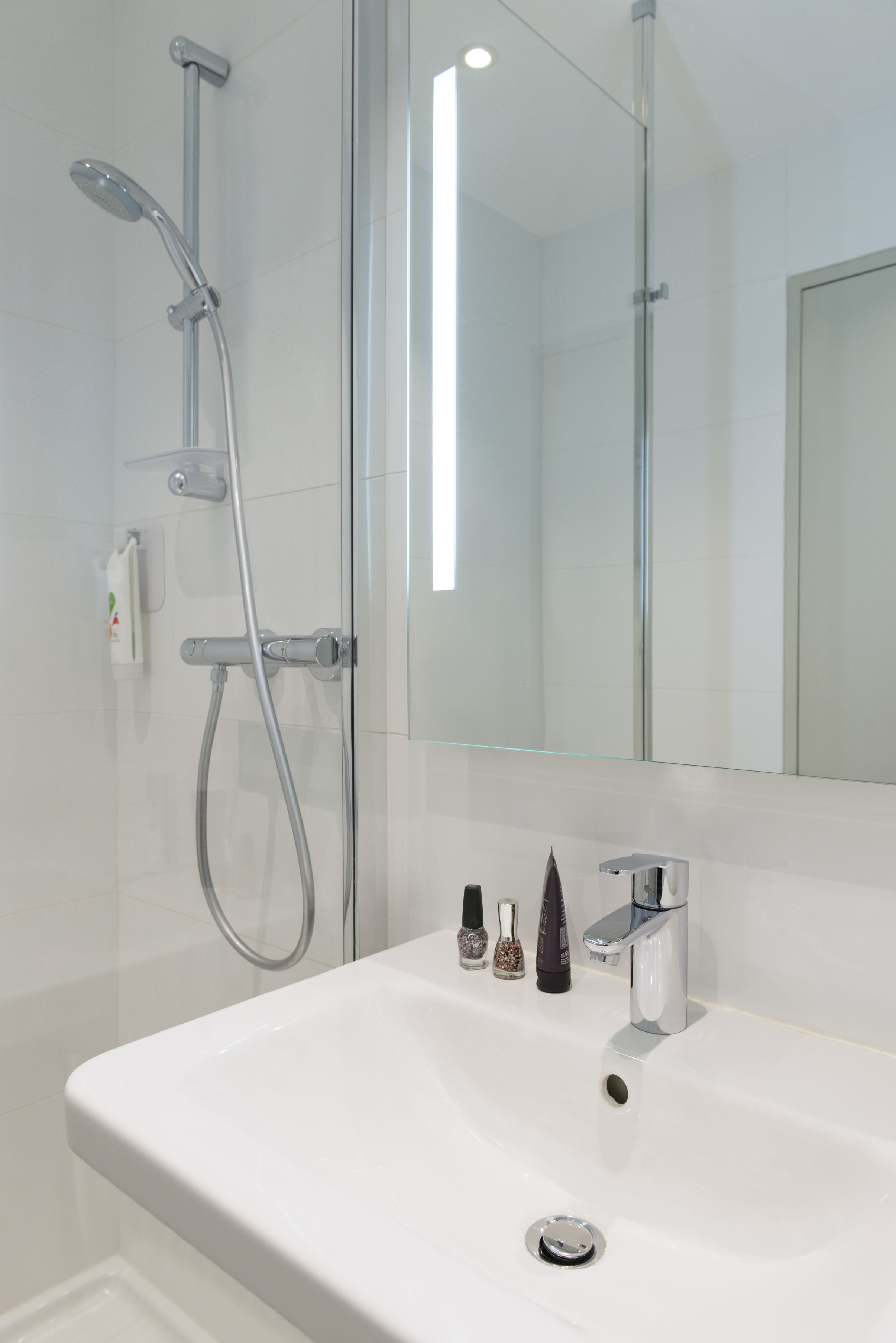 Un baño moderno con cabina de ducha de vidrio, lavamanos blanco y un espejo grande.