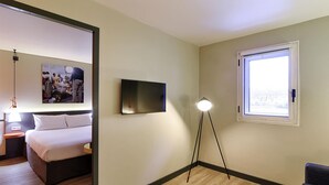 Una habitación de hotel con cama, televisor de pantalla plana, lámpara de pie y ventana.
