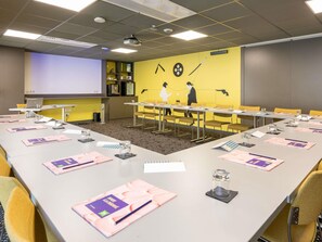 Une salle de conférence équipée d’une longue table, de chaises, d’un écran de projection et d’un mur orné d’une fresque.