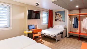 Een hotelkamer met een bed, een bureau met stoel, een televisie, een kledingkast en een raam met jaloezieën.