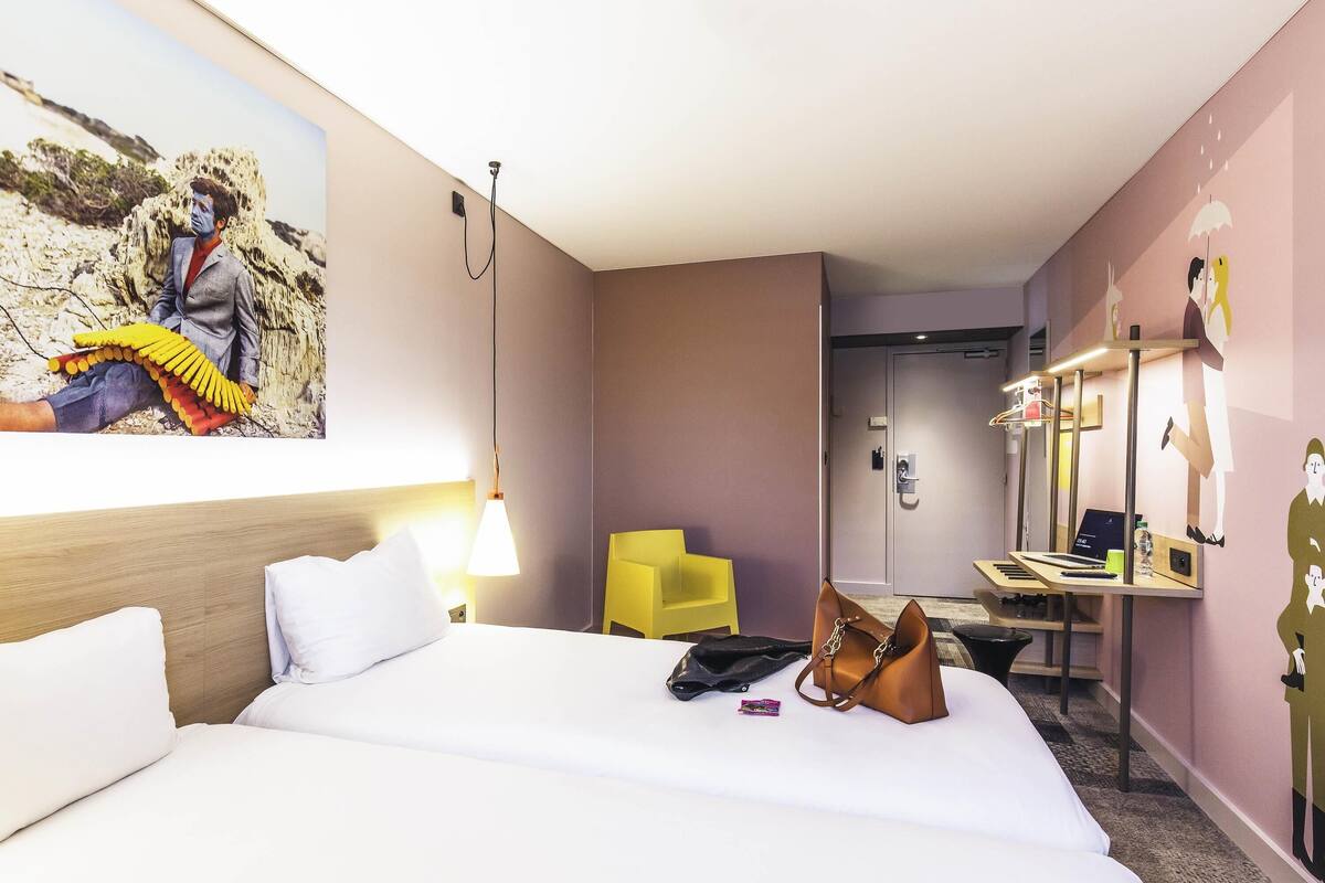 A hotel room with a bed, a desk, a chair, and a painting on the wall.