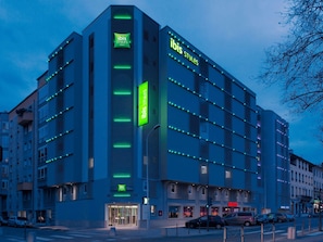 Ein mehrstöckiges Hotel mit modernem Design, mit einem gut sichtbaren 'ibis Styles'-Schild, einem Glastürbereich und einem Parkplatz davor.