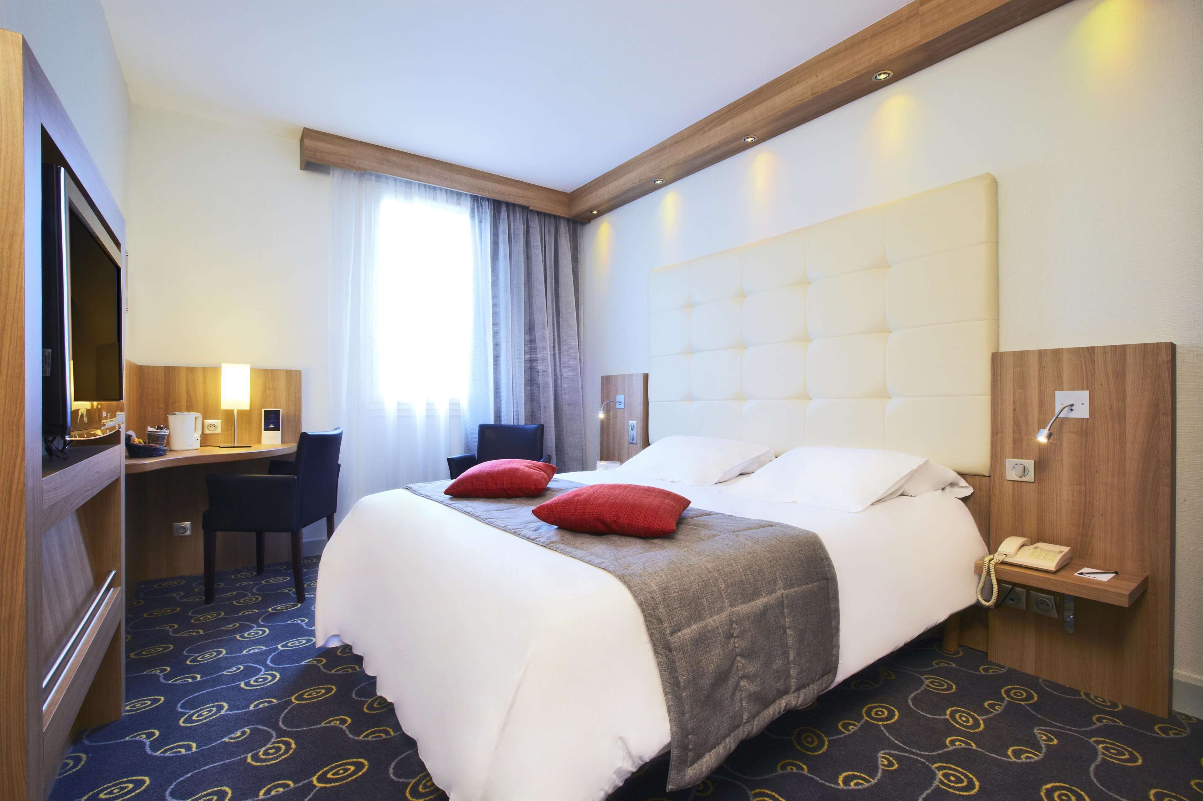 A hotel room with a bed, desk, chair, and a telephone.