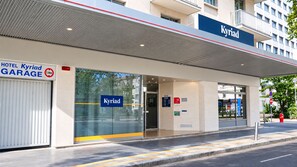 Entrada de hotel com placa de garagem, sinalização 'Kyriad' e hidrante.