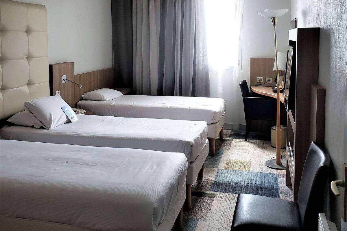 Habitación de hotel con dos camas, un escritorio, una silla y una lámpara.