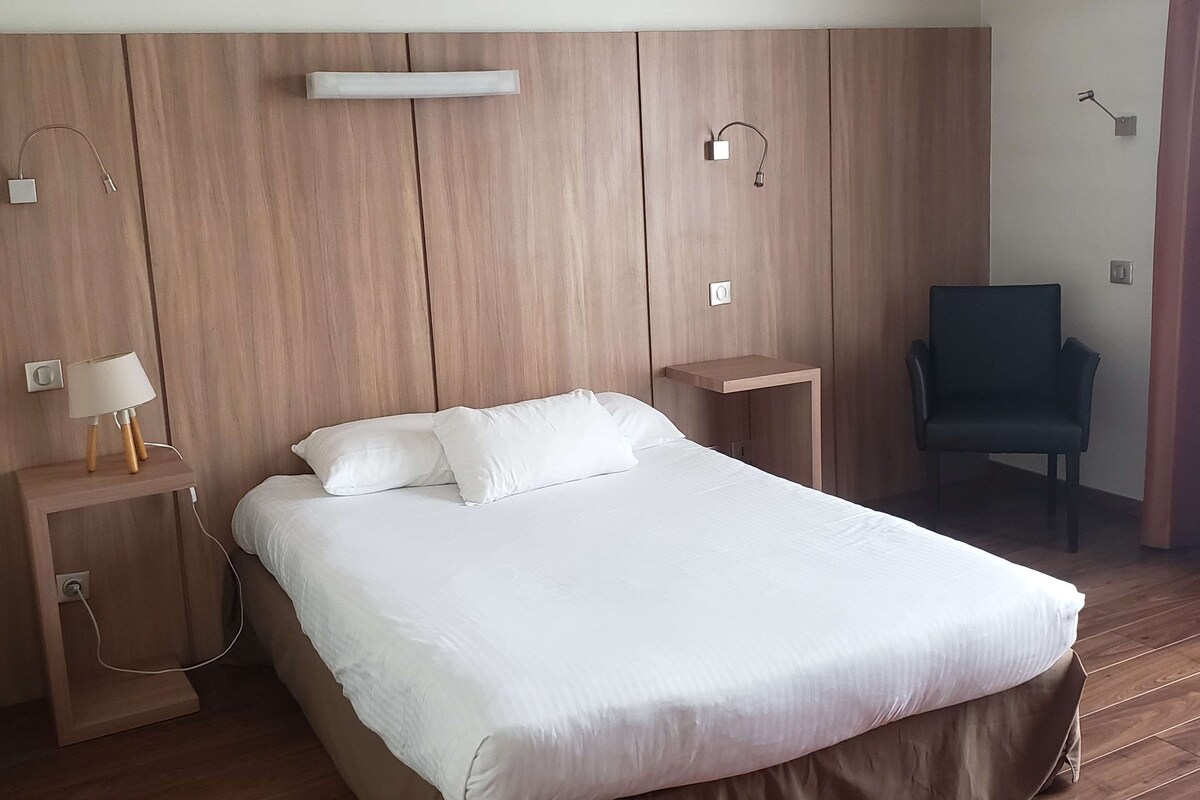 Une chambre d’hôtel moderne avec un grand lit, des panneaux de bois au mur, un bureau avec une lampe et un tapis rouge.